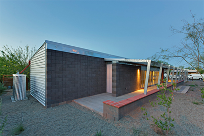 Photograph of a one-story house with a long south-facing wall made of tiles and shaded by a sunscreen.