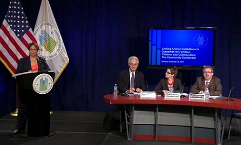 Photograph of a woman (Sherone Ivey) standing at a podium to the left of a table where two men (Ted Howard and Charles Rutheiser) and a woman (Sarah McKinley) are seated.