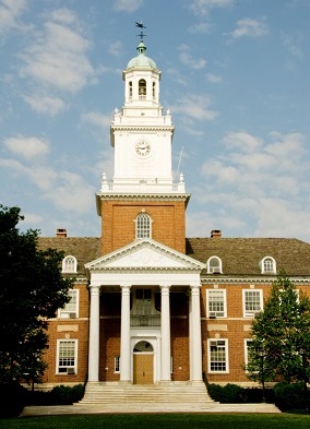 Photograph of the main entrance to one of the buildings at Johns Hopkins University. The entrance to the three-story brick neo-Colonial building is marked by a two-story portico and a three-level brick-and-wood tower.