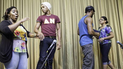 Photograph of four participants in a community theater performance on a stage in front of a curtain.