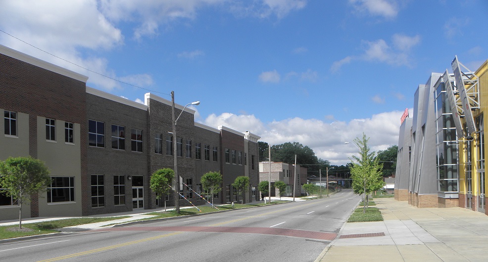 A photograph taken at street level up a four-lane street. On the right side of the picture is a landscaped sidewalk passing in front of the new Stax Museum of American Soul Music. On the left side of the picture and across the street are the two-story brick façades of two commercial buildings, the Towne Center at Soulsville USA.