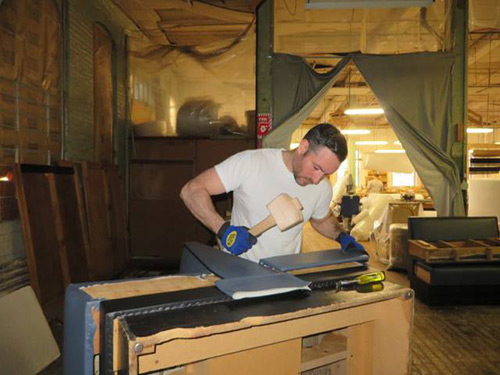 Photograph of a worker re-upholstering a bench in a workshop.