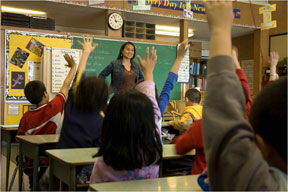 Children in class with hands raised, ready to answer their teacher’s questions.