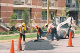 Three workers repairing a road in front of new townhouses 