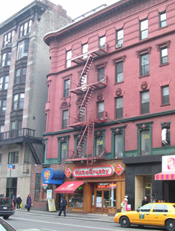 Photograph of red brick five-storey apartment with commercial businesses on a New York City street.