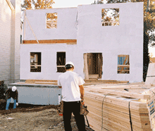A photograph of two men standing in front of a house under construction.